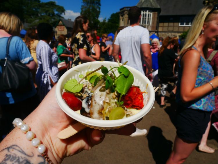 Taken from her perspective, Kacie holds up a bowl of street food at a busy festival