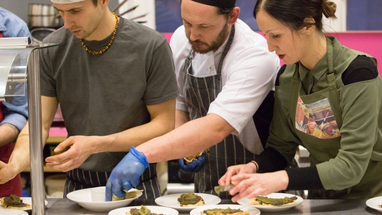 Three chefs are putting the finishing touches to several plates of food
