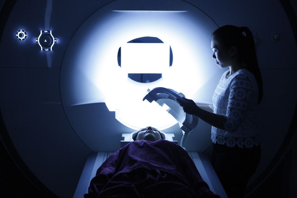 Mae gwyddonydd yn paratoi claf benywaidd ar gyfer sgan MRI