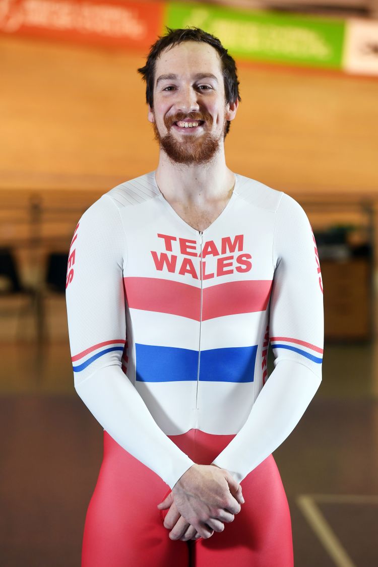 Photograph of Lewis Oliva standing in his Team Wales kit at the Newport Velodrome.