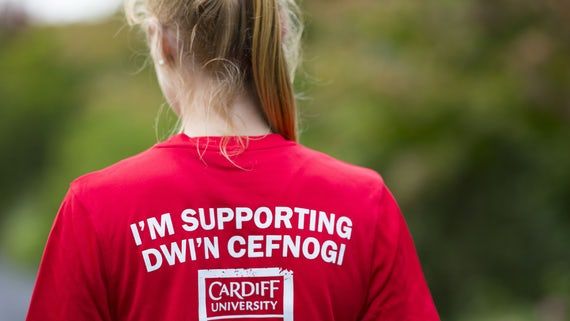 A girl in a red t-shirt faces away from the camera. On the back of her t-shirt is the Cardiff University logo and the words I'm Supporting